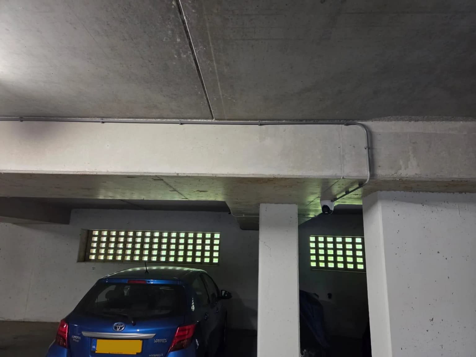 Dome camera strak gemonteerd onder betonbalk met zicht op parkeervakken in VvE Ede